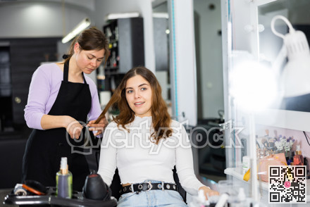 Female hairdresser cuts the hair of a young woman client