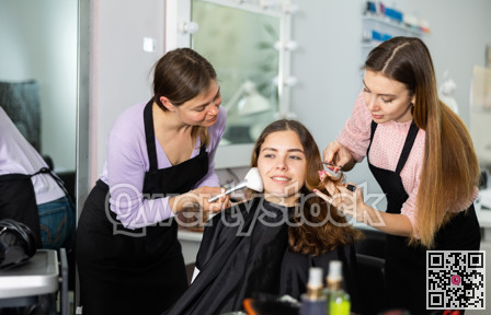 Professional female stylists making hairstyle and makeup to young woman