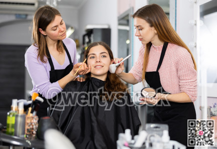 Professional women makeup artists applying shadows and blush to young client