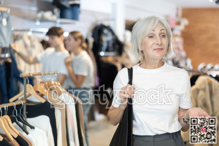 Old woman watching excitedly large stock of clothes in clothing store