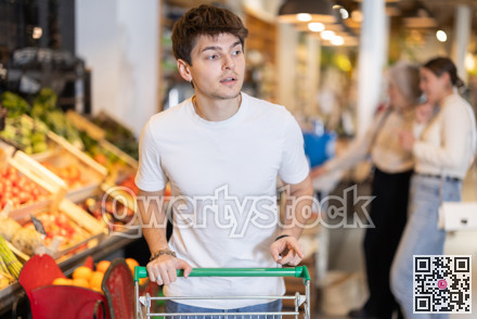 Young guy with shopping cart chooses groceries