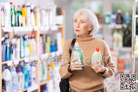 Elderly female customer diligently picking out dishwashing liquid