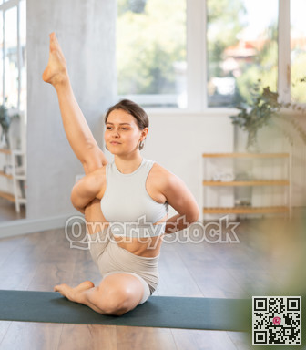 Sports experienced girl yoga teacher performs compass pose, parivritta surya yantrasana on mat in yoga studio