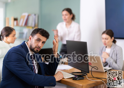 Young woman standing and scolding sad seated colleagues in office