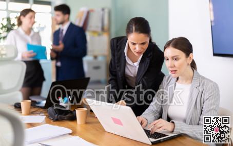 Young girl helping colleague with tasks on laptop