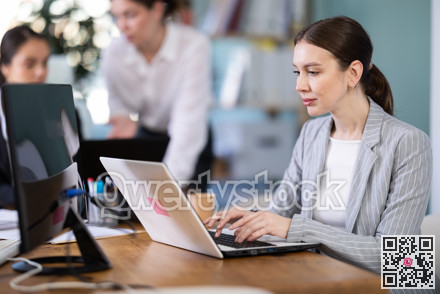 Focused young woman working on laptop during busy corporate session
