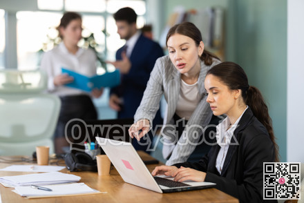 Young woman helping female colleague work on laptop