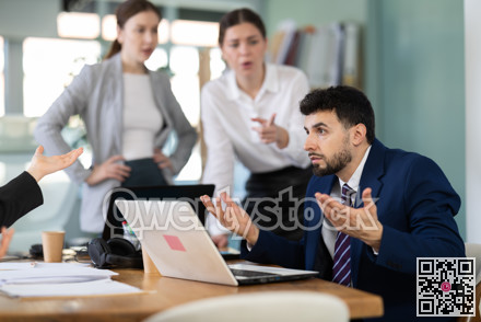 Frustrated man sits at a table with a laptop in front of his colleagues in office