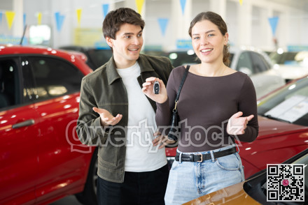 Young couple holding keys to new car in dealership