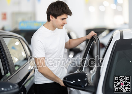 Guy checking, examining new car before making purchase in dealership. man look at auto and touch it