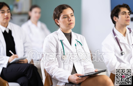 Young girl medical student dressed in labcoat sitting and listening lecture, taking notes on tablet in lecture hall