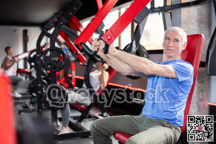 Mature man doing triceps curls in exercise machine during strength training in gym