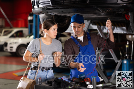 Guy mechanic checking woman client's car with measuring device