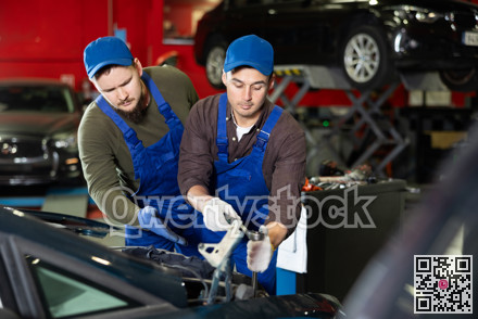 Skilled male auto mechanics in blue overalls repairing automobile
