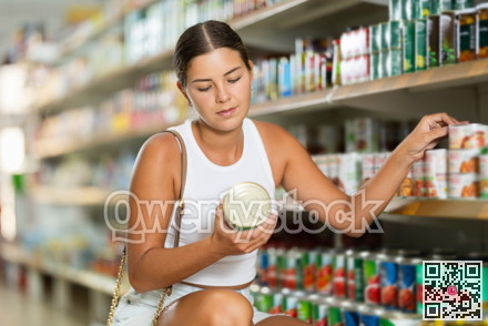 In supermarket store, woman choose jar of canned food
