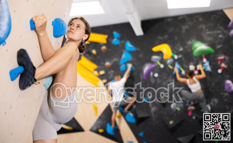 Motivated girl climbing without ropes on artificial bouldering wall