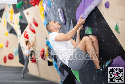 Male climber ascending colorful holds on indoor bouldering wall