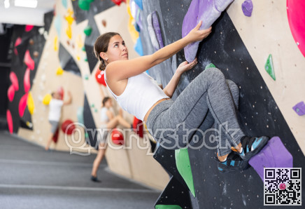 Young woman climbs steep artificial wall in sports complex and trains endurance