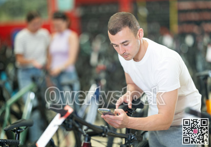 Focused man photographing bikes with smartphone in store