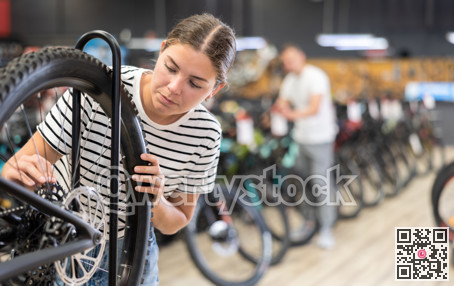Attentive young female buyer examining bicycle wheel in store