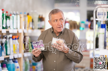 Elderly male shopper chooses scented candles in supermarket for romantic evening