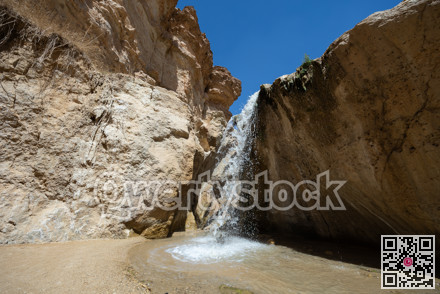 Small waterfall cascading into serene pool within oasis of Tamaqzah, Tunisia, surrounded by rugged cliffs