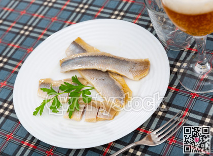 On table is plate with appetizer - salted Atlantic herring fillet decorated with parsley