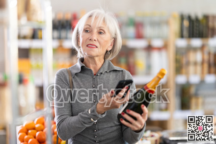 Checking expiration date of sparkling wine - elderly female shopper scans QR code on label of wine using smartphone