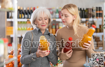Girl and grandmother buyers examine good, doubt and choose between varieties of fruit juice in store