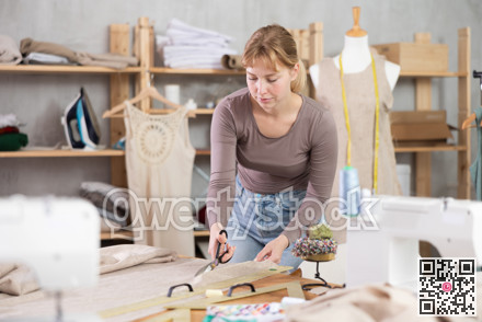 Young female dressmaker cutting textile in sewing workshop