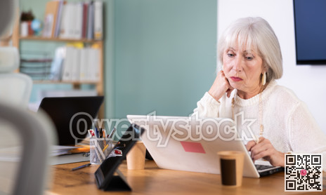 Senior woman working in office, using laptopat workplace.