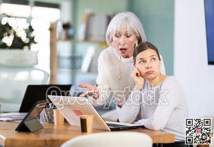 Female mature boss yells at woman employee, staff work at computer