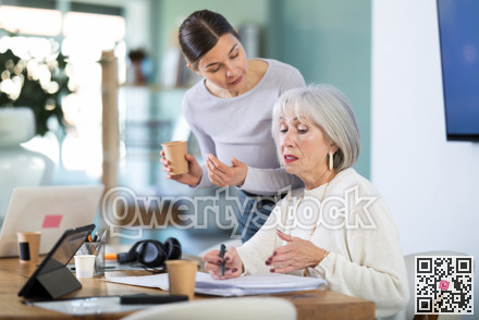 Elderly woman taking notes in document adult colleague helps