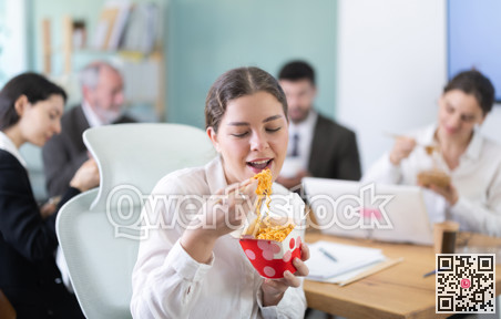 Lunch break - woman eating noodles with colleagues in modern office