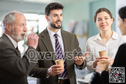 Group of positive office workers drink coffee and chat during work break in office of business company