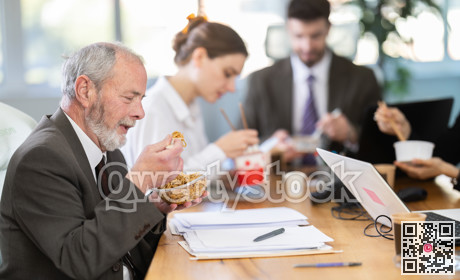 Lunch break - mature man eating noodles with colleagues in modern office