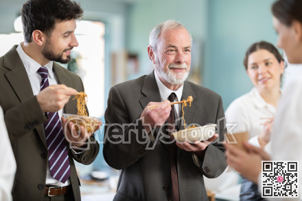 Group of colleagues, man and woman, are having lunch in office during their break, eating noodles