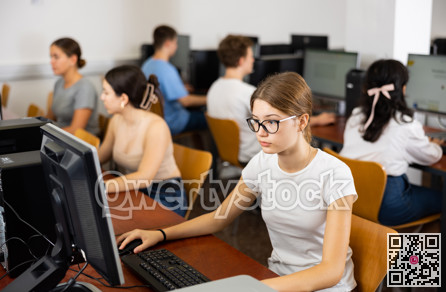 Interested young female student with glasses working on computer in library, looking for necessary information on Internet