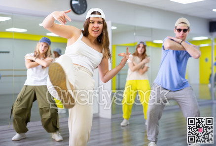 Ordinary teen girls and boy performing kick step movement during training together in dance school