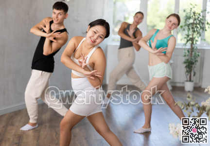 Sporty girl and guy practicing energetic dance moves with group in choreography class