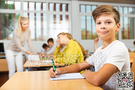 Boy listening to lecturer and writing in notebook in classroom