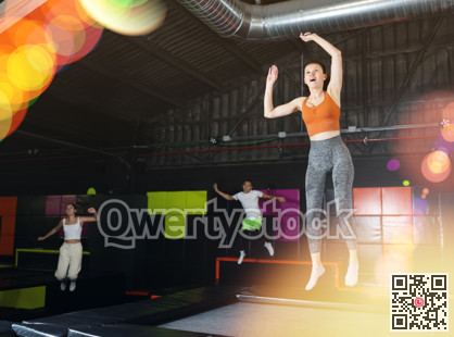 Happy middle aged woman practicing and jumping on trampolines in a sports indoor center, workout and modern entertainment concept