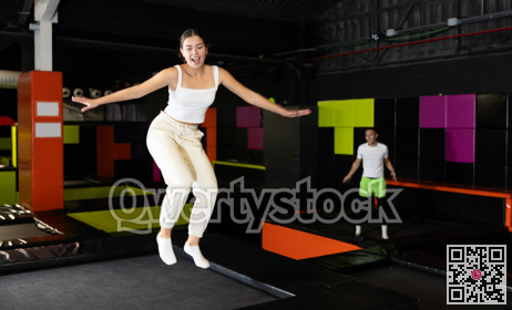 Girl acrobatic athlete jumping and exercising on trampoline indoors, modern hobby and fitness concept