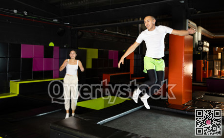 Joyful young man jumping on trampolines in colorful amusement park