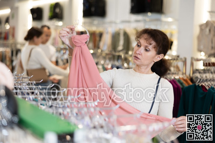 Middle-aged woman choosing thin scarf in clothing store