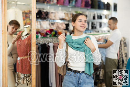 Young girl choosing thin scarf in clothing store