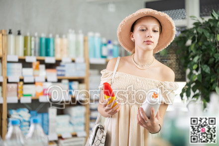 Female shopper in summer clothes and hat chooses sunscreen at pharmacy