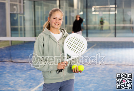 Positive teenage girl looking at camera while playing padel at court