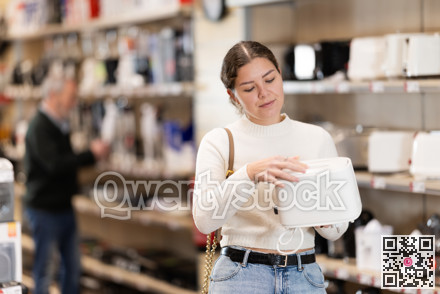 Positive young woman choosing toaster in hypermarket