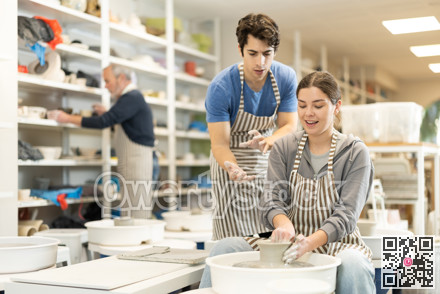 Young man helping young woman shape pottery on wheel